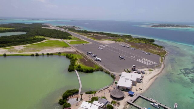 Aerial drone rising over Los Roques airport, showing small planes, lagoon, boats, and Caribbean Sea in Venezuela.