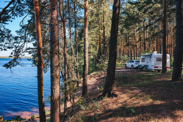 Caravan RV parked on the beach under a trees facing blue sea, lake or river. Family traveling with motorhome. Travelers on an active family vacation.