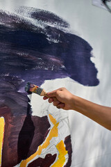 Close-up of young adult hand painting abstract art on canvas. Bright sunlight casts shadows,...