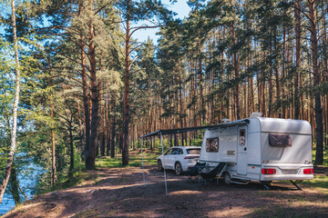 Caravan RV parked on the beach under a trees facing blue sea, lake or river. Family traveling with motorhome. Travelers on an active family vacation.