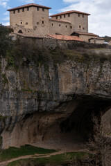 Medieval orbaneja del castillo dominating a rocky cliff over a cave in burgos, spain