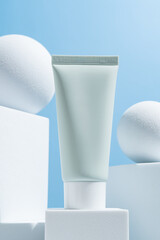 green cosmetic tube on a blue background on white cube podiums. The concept of a cream with natural ingredient and not testing on animals.