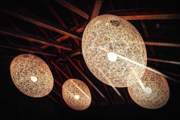 Artistic woven pendant lights on wooden ceiling.