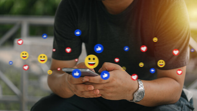 Man using smartphone with social media emojis floating, representing likes, hearts, and emojis. Perfect for digital marketing, social engagement, or online communication concepts.
