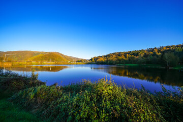 View of the autumn landscape at Eiserbachsee in Rurberg. Idyllic nature at the Eifel Rursee in the Volcanic Eifel region of Rhineland-Palatinate.
