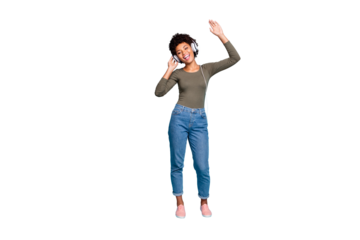 Full length photo of cheerful positive dark skin hipster girl listen music  use headset sing her favorite stereo melody song raise hands wear green pullover denim jeans isolated blue color background