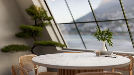 Coffee cup and flower vase on a grey marble round table next to a bonsai in a room with roof window.