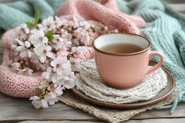 Cozy spring background with a pink cup of tea, a knitted blanket, and blooming cherry blossom flowers