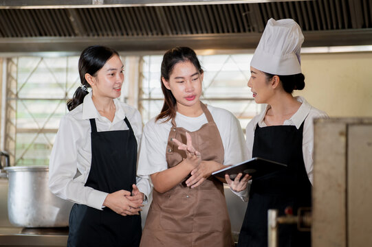 Asian female chef holding tablet and talking to students in front of a stove or oven in the kitchen - Powered by Adobe