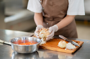 Close up of gloved hands chef cleaning white onion peels or skins on wooden chopping board.