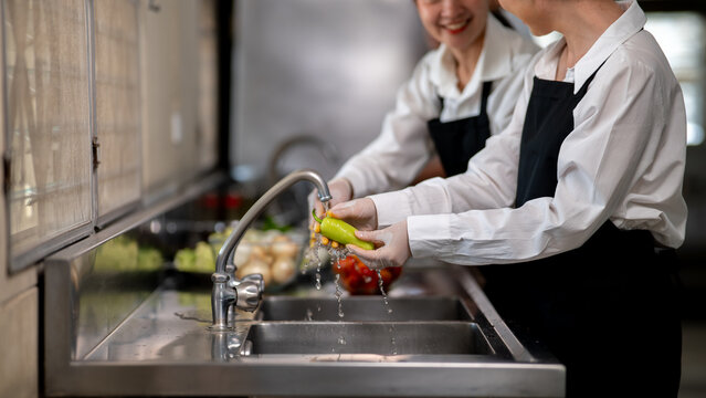 Asian female chefs is washing or cleaning a green pepper with tab water in restaurant's kitchen sink