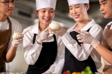 Close up of gloved hands female chef holding a peeled onion with students pointing their fingers.