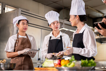 Female chef teaching her students or assistants how to use knife to cut a cabbage at kitchen counter