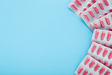 New blister packs of red capsule pills on light blue table background. Pastel color. Closeup. Empty place for text. Top down view.
