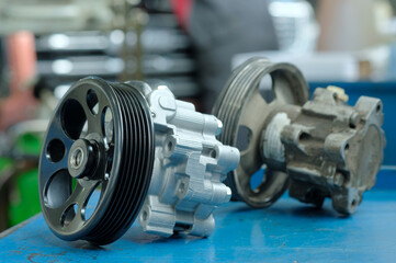 Car service.Spare parts.On the mechanic's desk are: a new power steering pump and a faulty one in the distance.Close-up.