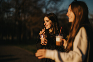 Two girls share a pleasant moment outdoors, sipping on beverages and enjoying the warm, golden glow of the sunset.