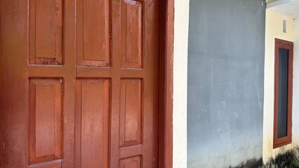 A simple reddish-brown wooden door with multiple panels stands next to a plain gray wall with a subtle white trim