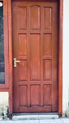 A simple reddish-brown wooden door with multiple panels stands next to a plain gray wall with a subtle white trim