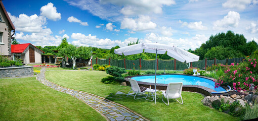 Beautiful landscape design of a country house with a well-groomed lawn, a swimming pool, an umbrella, chairs and a flowering bush. Lentious summer rest in nature.
