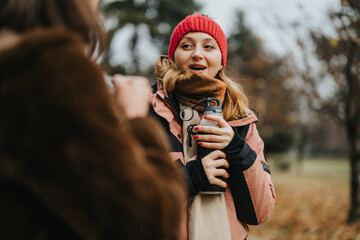 Two friends interact outdoors, focusing on one person warmly dressed with a scarf, red hat, and...