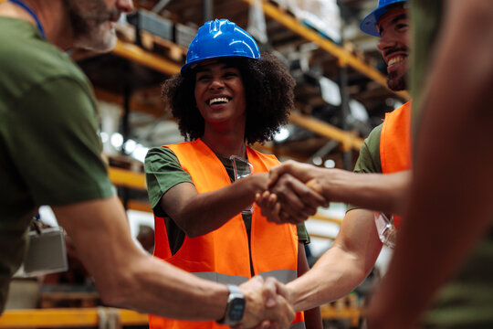 Happy workers shaking hands in warehouse, celebrating success