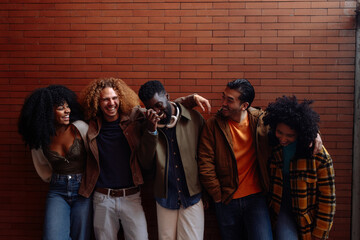 Group of diverse friends laughing together against brick wall