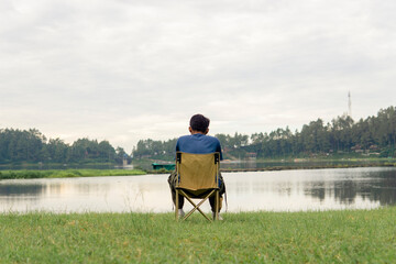 A young man sitting on a chair at lake with relaxing mood, lonely man, Asian man travel alone.