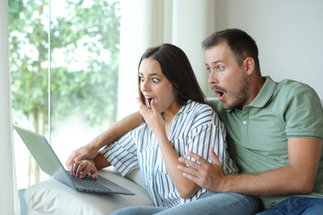 Surprised couple checking personal computer content at home