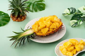 Fresh pineapple chunks served in a pineapple bowl on green table background.