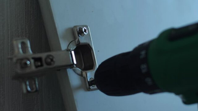 close-up of the process of assembling cabinet furniture, a kitchen assembler tightens door hinges with a screwdriver, tightening a screw macro