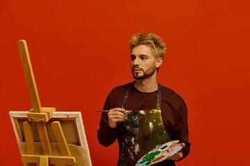 Handsome young man painting a vibrant canvas against a bold red backdrop in an artistic studio