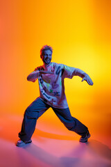 Dynamic young man showcasing dance moves against a vibrant orange and purple backdrop