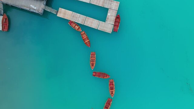 Drone video of Lago di Braies captured from above at sunrise. Wooden boats tied beside the rustic boathouse, surrounded by still water and pristine natural light