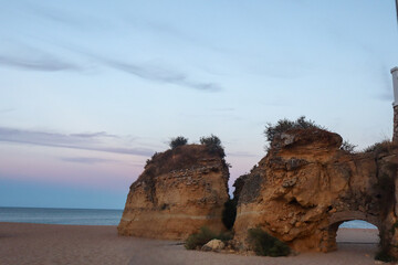 Golden limestone cliffs tower above turquoise waters on a sunny day in Lagos, Portugal, offering...
