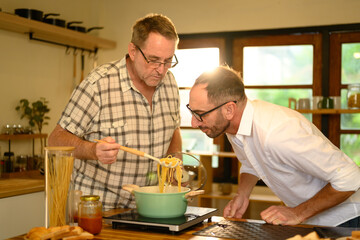 Happy senior man and grown son preparing pasta dish in a bright kitchen. Father day concept