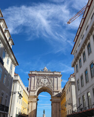 Lisbon’s iconic white archway at Santa Maria Maior frames yellow buildings and blue sky, a symbol...