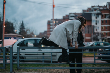 A woman dressed in a white coat leans over a metal railing, attempting to climb over it. The...