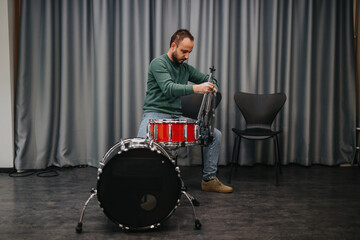 A person adjusts a drum set in a studio, preparing for practice. The calm setup indicates focus and...