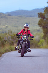 Front view of a beautiful, happy, smiling female motorcyclist riding leaning into a curve on a Harley-Davidson Sportster along a winding coastal road.