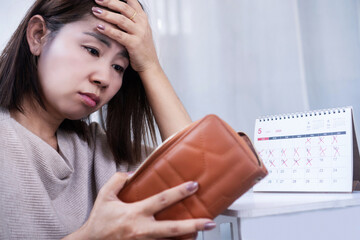 Asian woman feeling stressed while checking her empty wallet, worried about running out of money before the end of the month struggling with being broke and unable to cover expenses