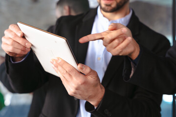 Close-up of unrecognizable businessmen in suits using a tablet and pointing at the screen ,while discussing work in a modern office environment with professional and collaborative atmosphere. 