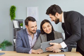 Young couple sitting at the desk discussing contract and having consultation with man realtor or financial advisor looking at tablet screen. Insurance agent consulting clients in office.