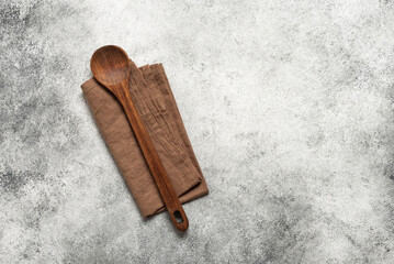 Wooden spoon and linen napkin on light grunge background, top view, flat lay