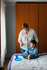 Mother giving food to disabled son with microdeletion syndrome at home