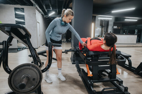 Fitness training session with a personal trainer assisting a woman with leg exercises in a state-of-the-art gym, showcasing teamwork and physical health. - Powered by Adobe