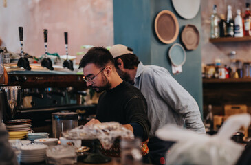 Baristas working in a coffee shop, preparing drinks in an aesthetically designed interior, featuring stacked cups, coffee equipment, and decor.