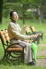 雨傘を持ってベンチに座り微笑む日本人の女性