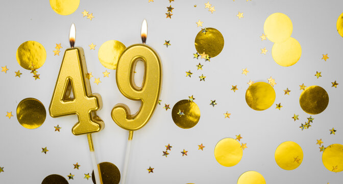 Burning Birthday candle number 49 on white background with golden confetti and glitter. Forty-nine years old. Happy Birthday. Card on festive background.