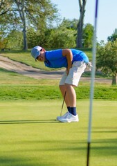 Young male golfer putting on green and bending over
