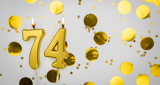 Number 74 golden celebration birthday candle on white with confetti background. Seventy-four years birthday. Concept of celebrating birthday, anniversary.